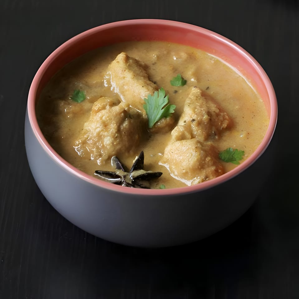 Creamy chicken curry with cilantro and star anise in a grey bowl with a pink rim.