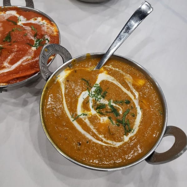 Two bowls of Indian curry, one orange with cream swirls and herbs, the other red, on a white table.
