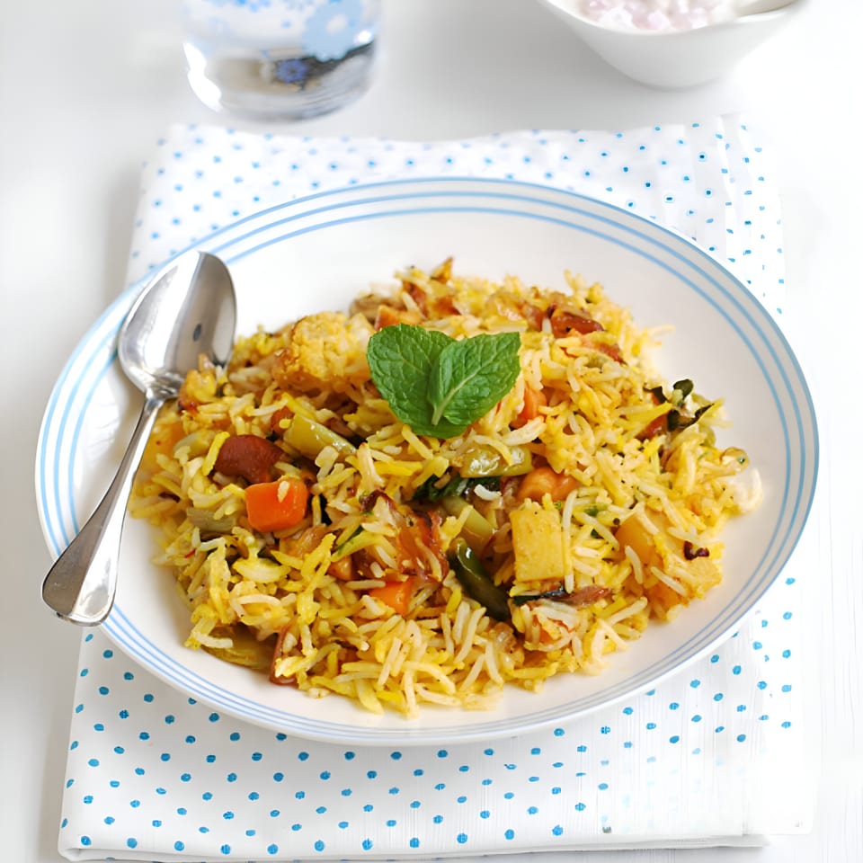 A white plate with blue stripes holds vegetable biryani, garnished with a mint leaf, on a polka dot napkin.