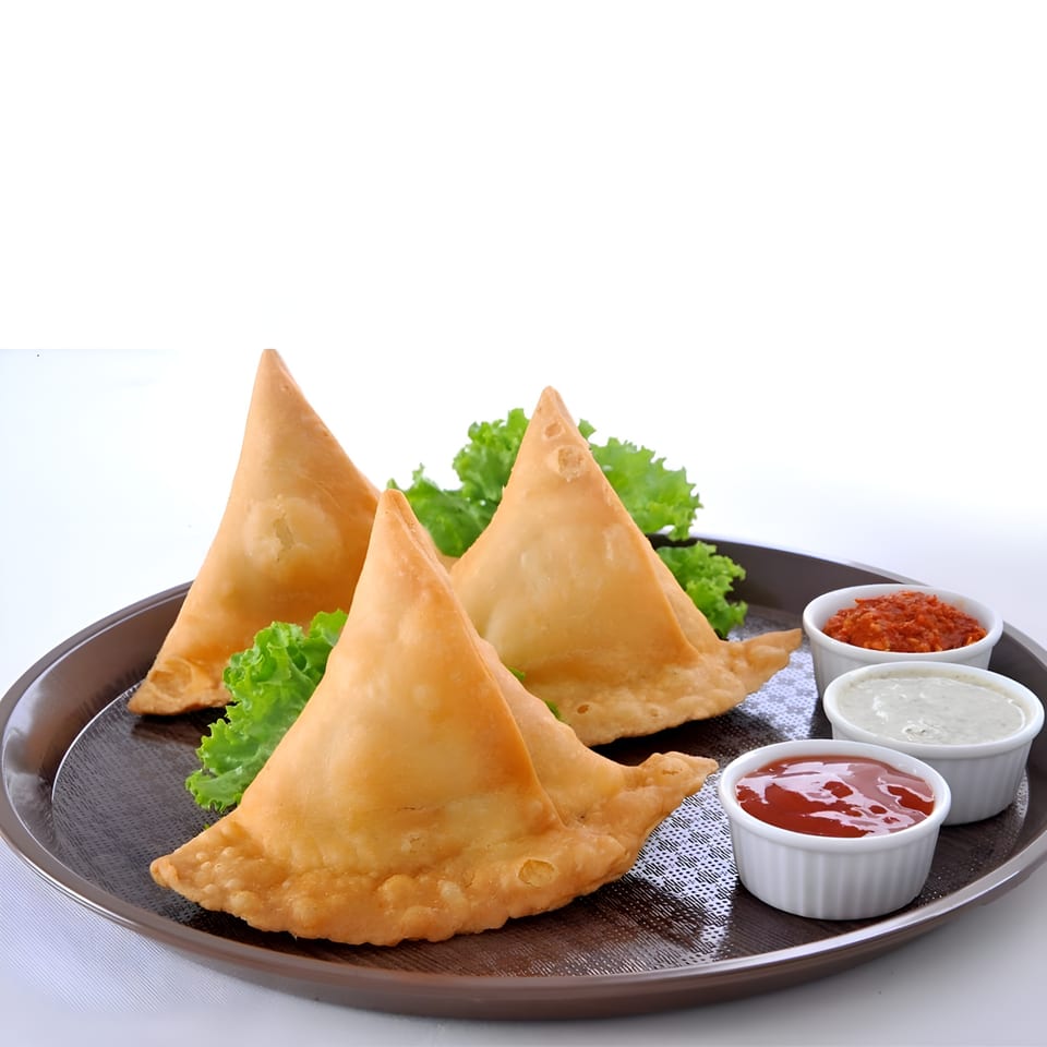 Three golden-fried samosas with lettuce garnish and three dipping sauces on a brown tray.